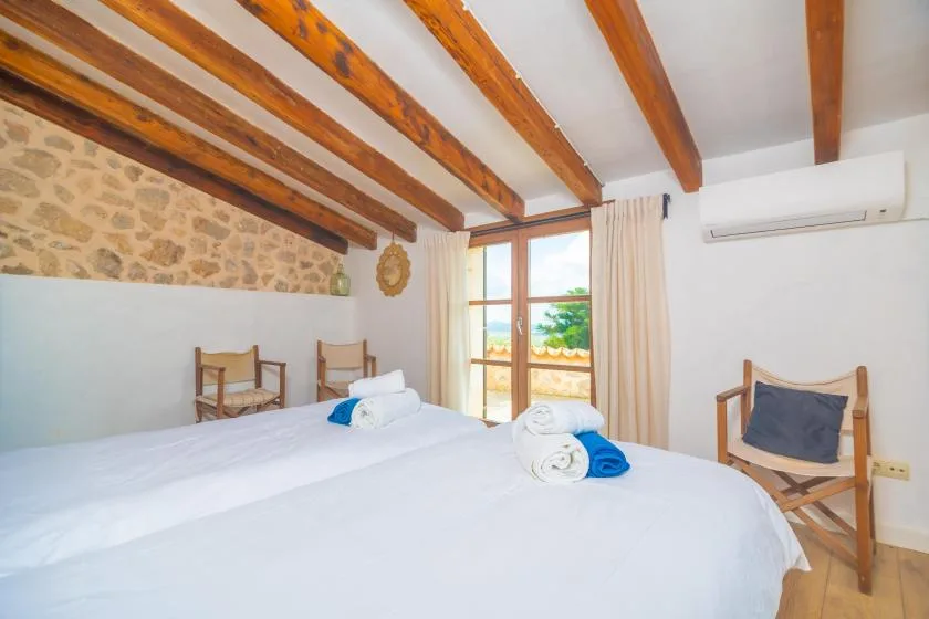 A bedroom with white bedding, exposed wooden ceiling beams, and a glass door.