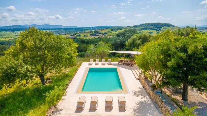 An outdoor swimming pool and lounge seating sit amid green countryside.
