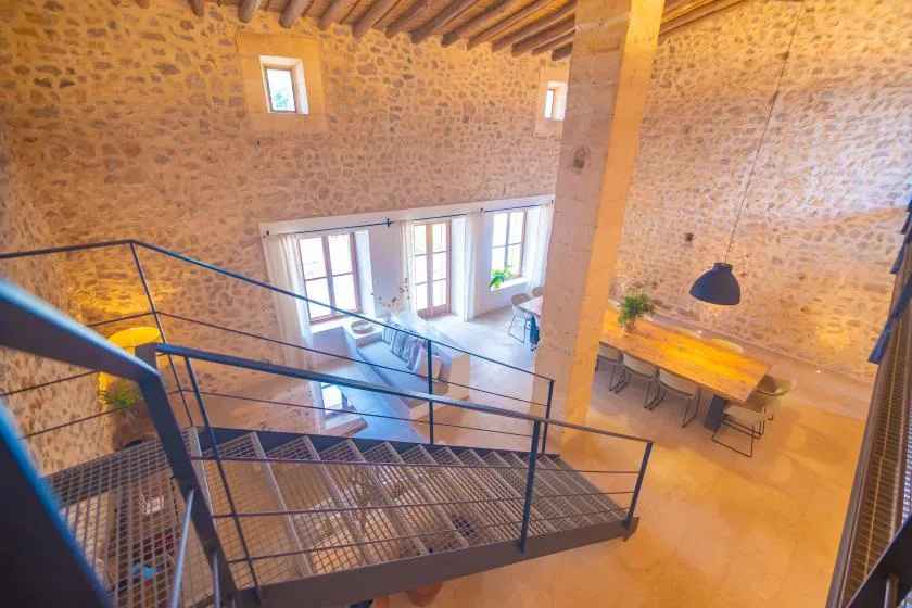 A stone-walled interior with a dining table and metal staircase.