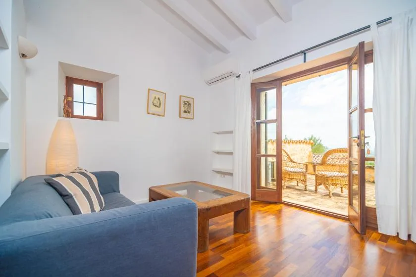 A living room with blue seating and open wooden doors leading to a sunny terrace.