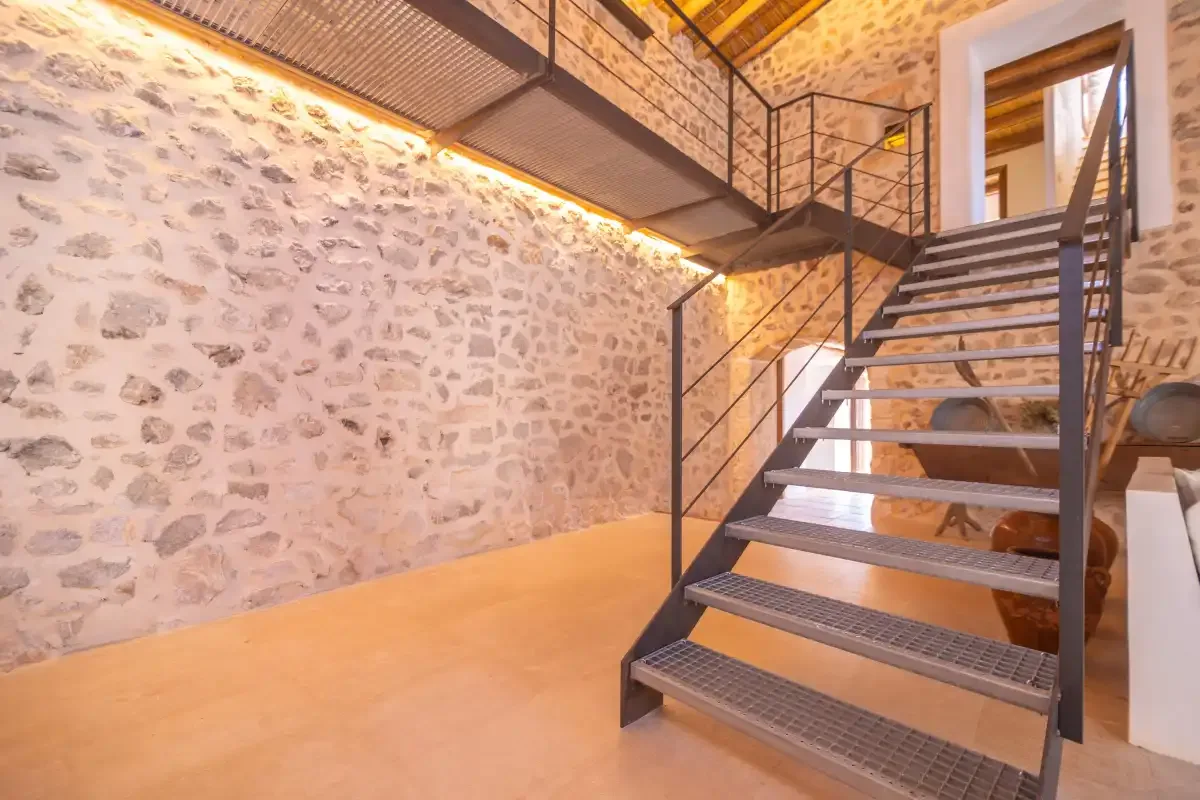 An interior stairway with open steps leads to an upper landing beside a stone wall.