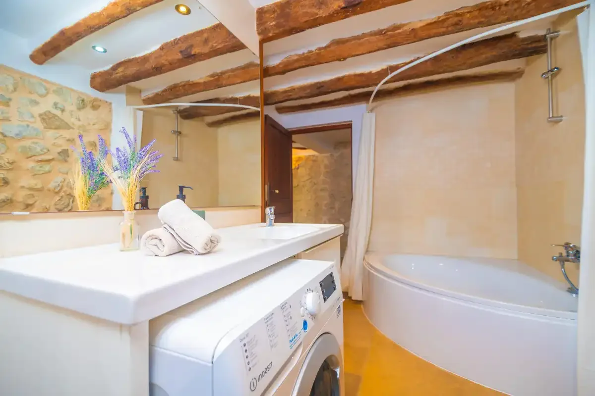 A bathroom with a bathtub, sink, and washing machine beneath exposed wooden beams.