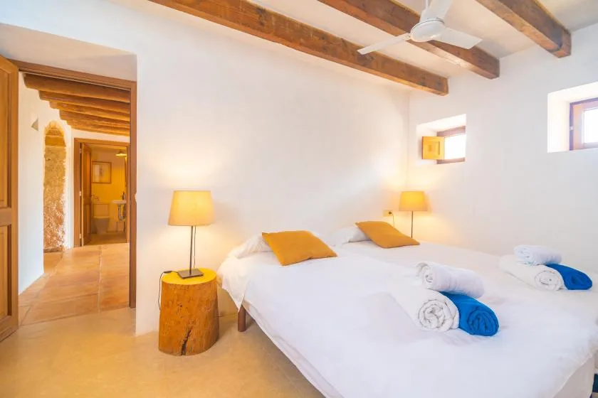 A bedroom with two beds, bedside lamps, and exposed ceiling beams.