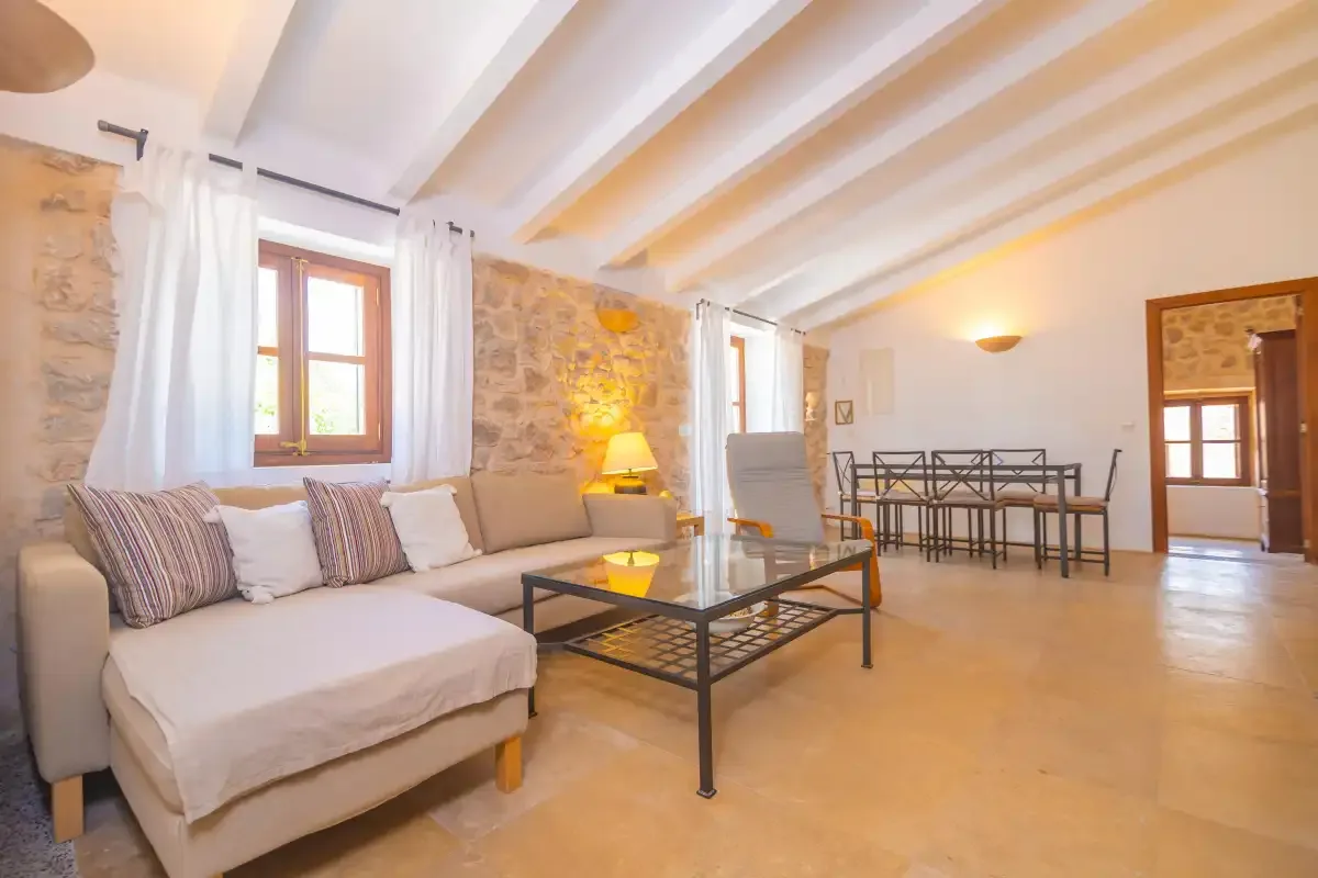 A bright living and dining area features seating, a coffee table, and exposed stone walls.