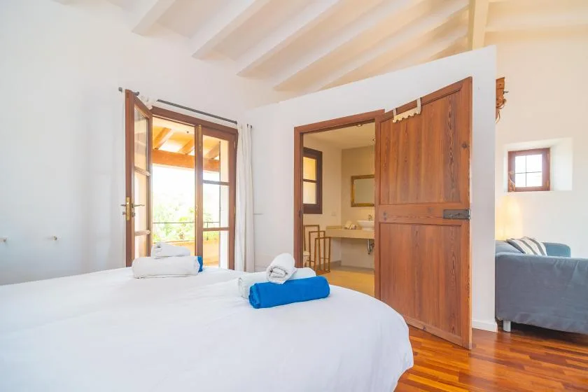 A bright bedroom with a white bed and an open wooden door to the adjoining room.