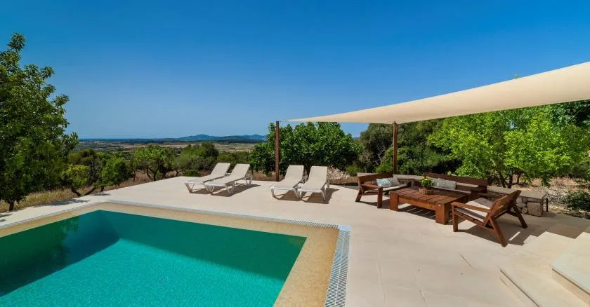 An outdoor swimming pool beside a shaded patio with lounge seating and a dining table.