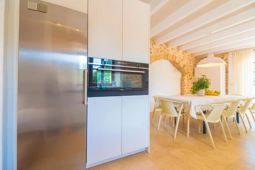 A bright kitchen opens onto a dining area with a long table and chairs.