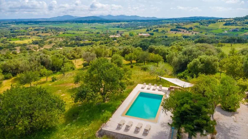 Aerial view of a swimming pool amid green countryside and distant hills.