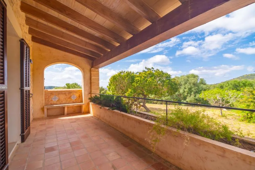 A covered terrace with tiled flooring overlooks green trees and open countryside.