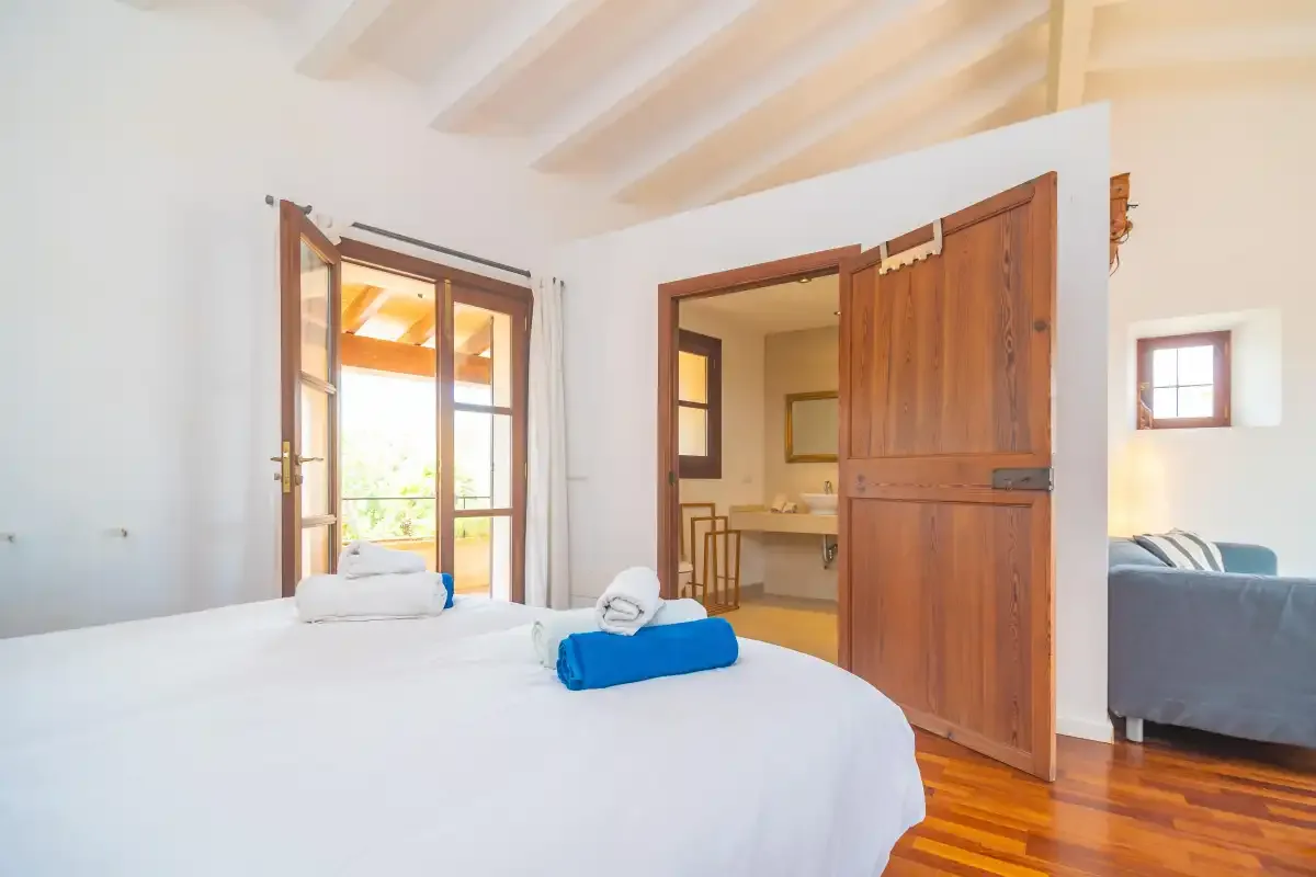 A bedroom with white bedding and an open wooden door leading to another room.