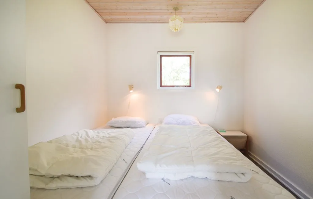 A bright bedroom with two beds beneath a small window.