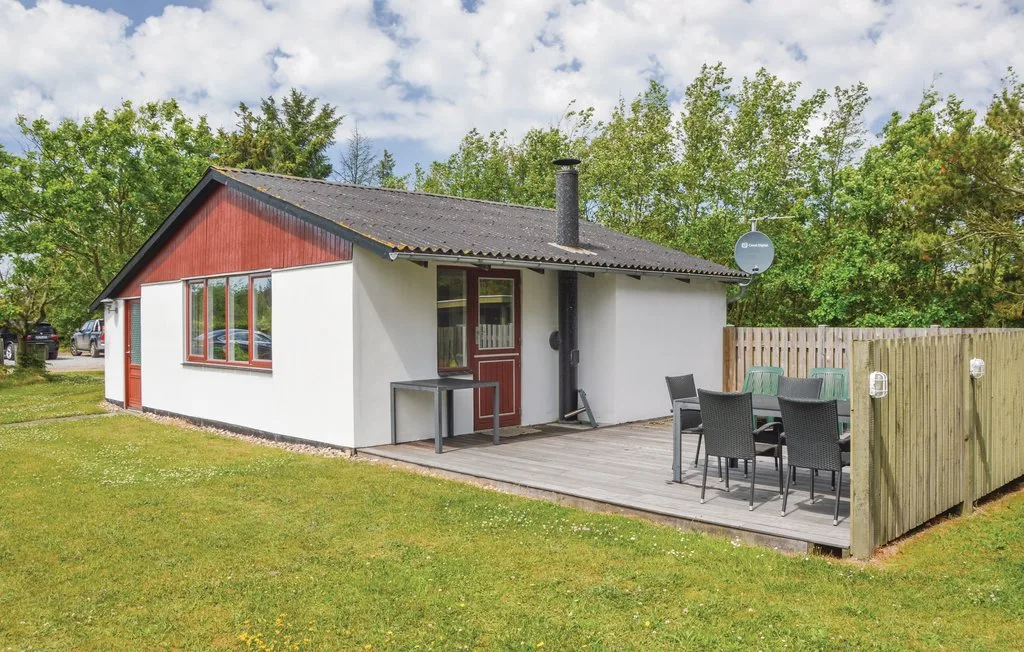 A small cottage with a wooden patio and outdoor dining area sits in a grassy yard.