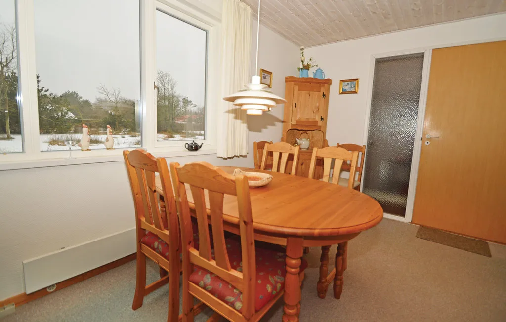A dining room with a wooden table and chairs beside large windows.