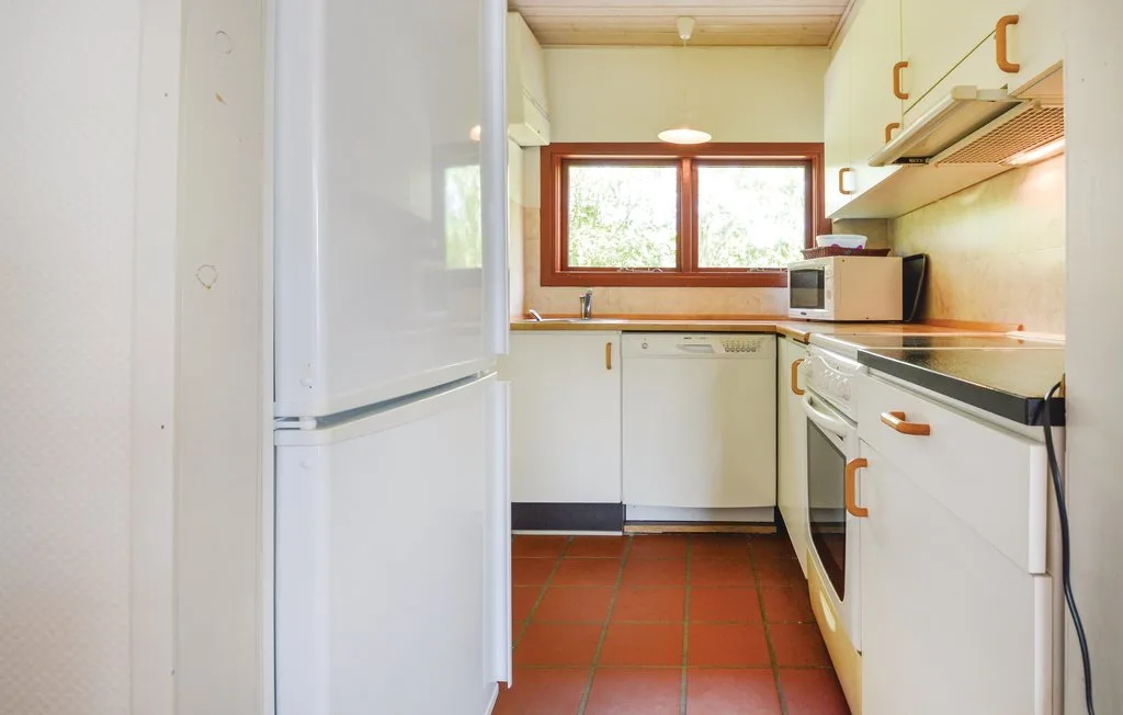 A compact kitchen with white cabinets, a refrigerator, and a window above the sink.