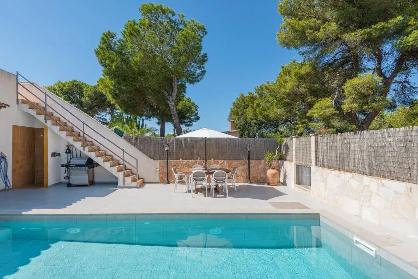 An outdoor swimming pool beside a paved patio with a dining table and seating.