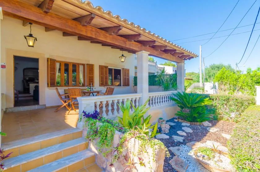 A covered patio has a dining table, wooden seating, and plants along the balustrade.