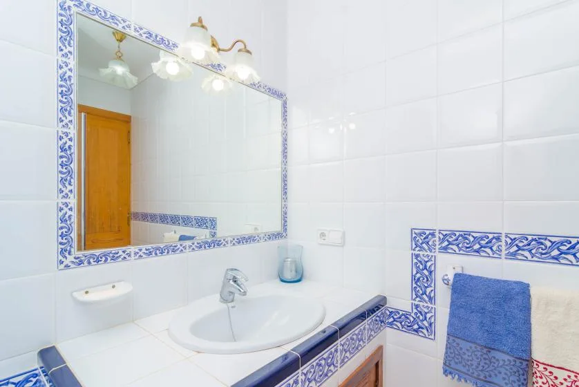 A tiled bathroom with a sink, wall mirror, and blue decorative borders.