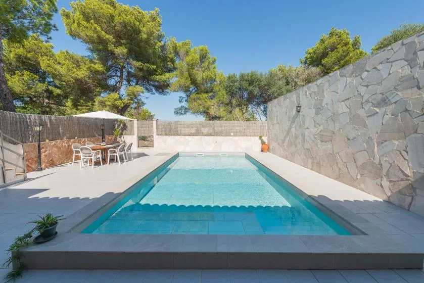 An outdoor swimming pool sits beside a stone wall and patio seating.