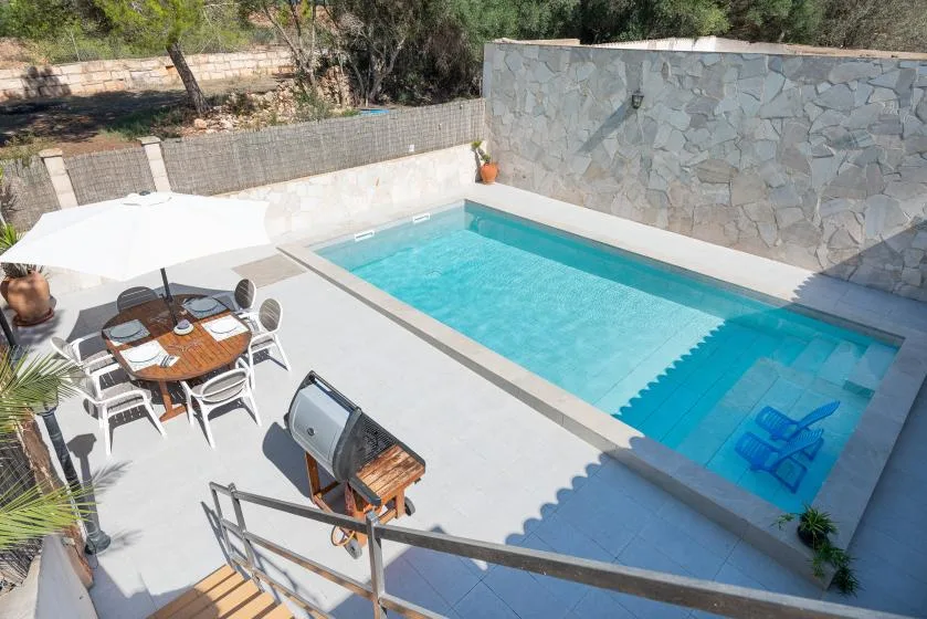 A swimming pool beside a paved patio with outdoor seating and an umbrella.