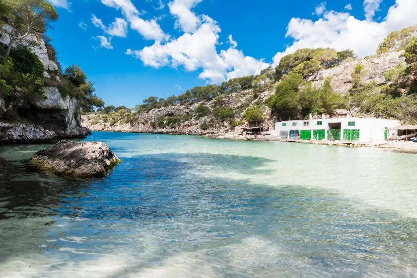 A clear turquoise inlet lies beneath rocky, tree-covered cliffs.
