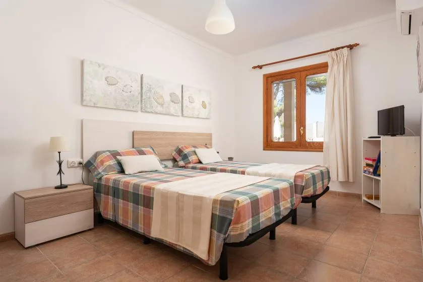 A bright bedroom with two beds and a wooden-framed window.