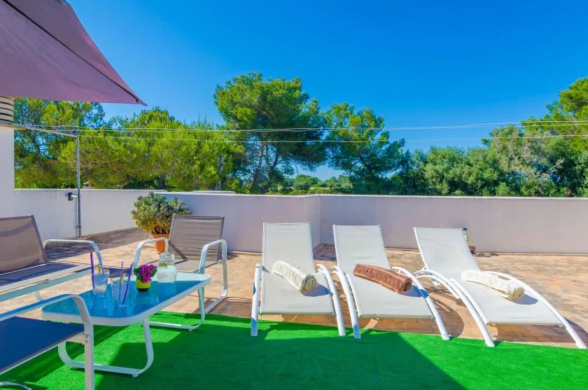 An outdoor terrace has white reclining loungers beside a small table.