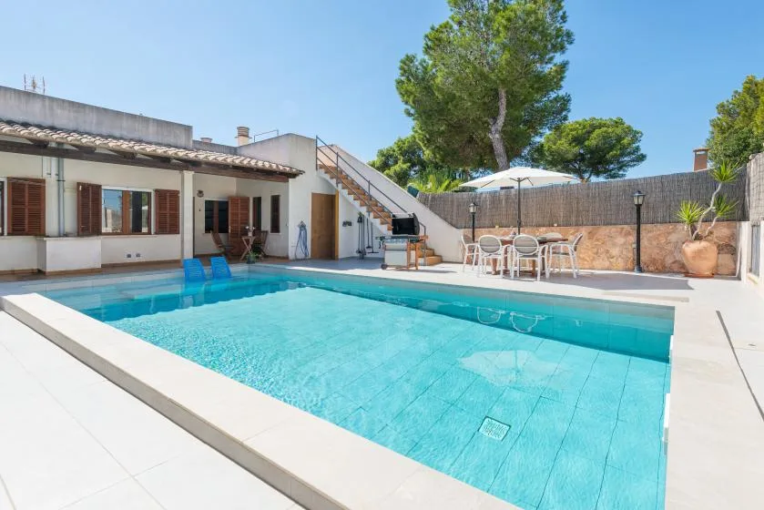 A swimming pool beside a white building, with outdoor seating and trees.