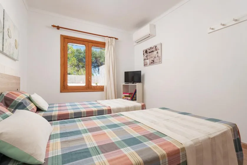 A bedroom with two beds covered in plaid bedding and a window.