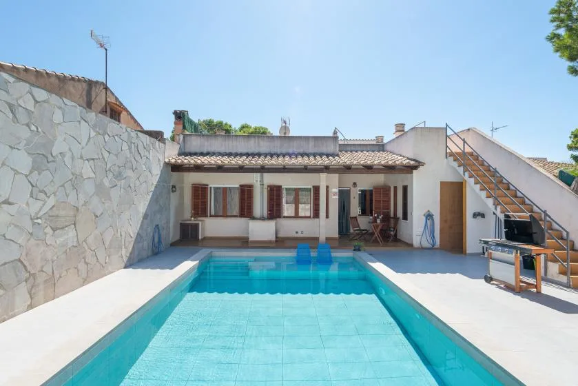 A swimming pool sits in front of a low building in a sunny courtyard.