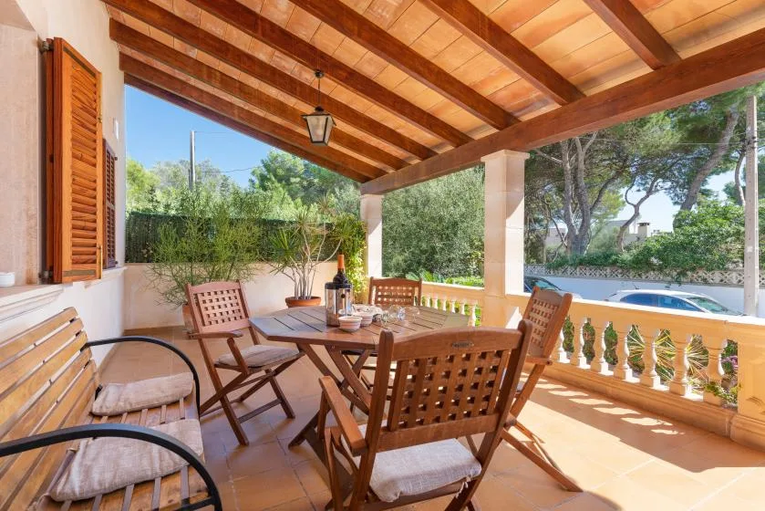 A covered outdoor dining area with a wooden table and seating overlooks greenery.