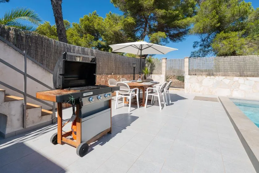 An outdoor patio with a barbecue grill, dining table, and umbrella beside a pool.