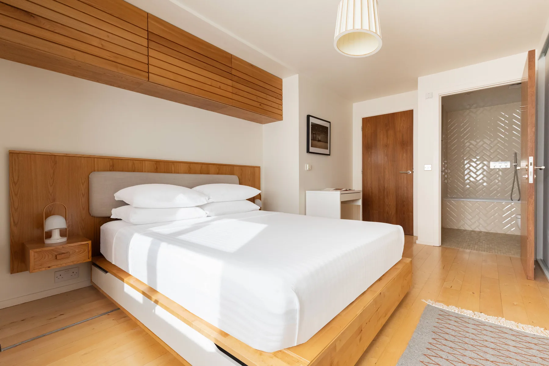 Un dormitorio luminoso con una cama bien hecha y suelo de madera.