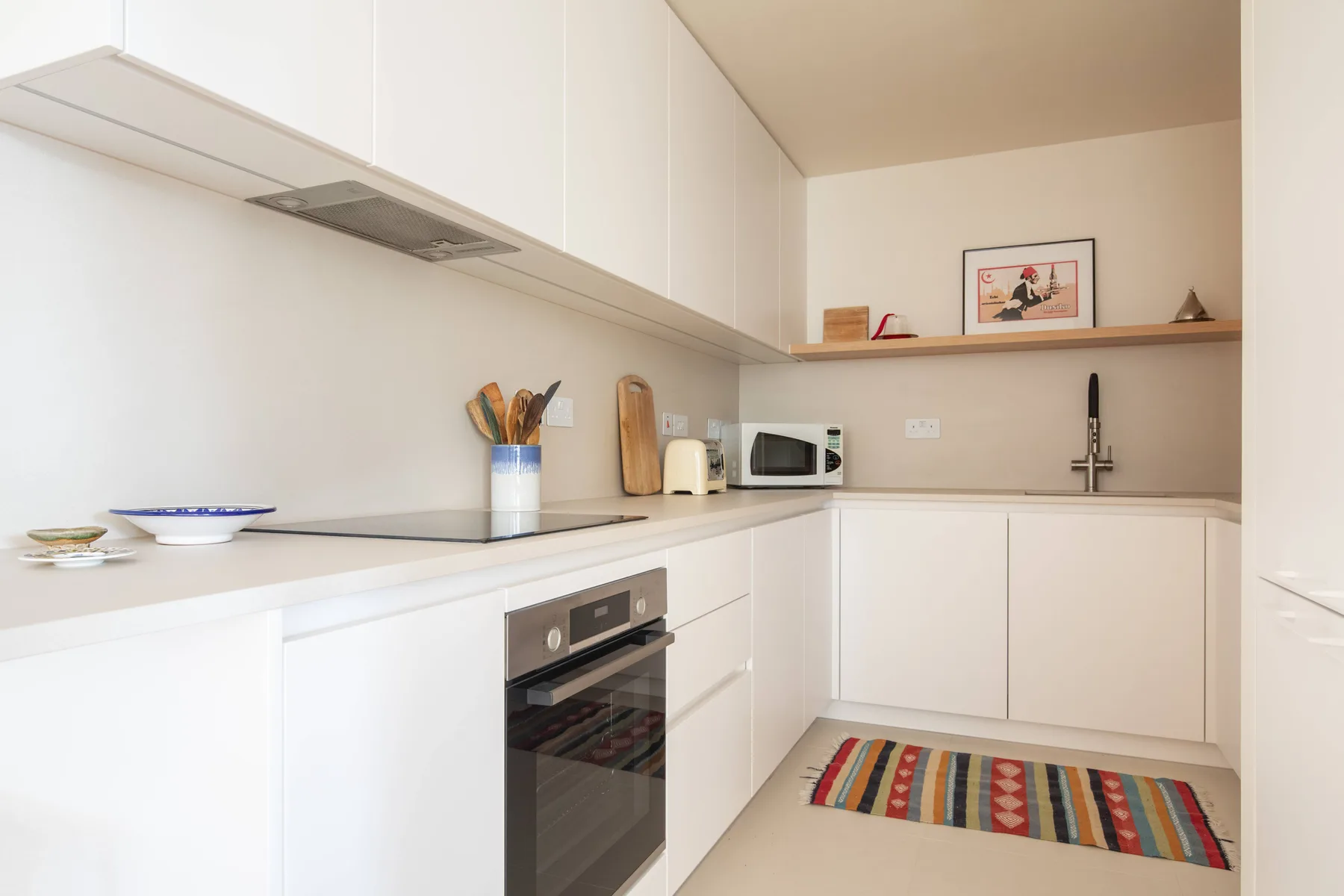 Una cocina moderna y luminosa con gabinetes blancos, encimera y una alfombra a rayas.
