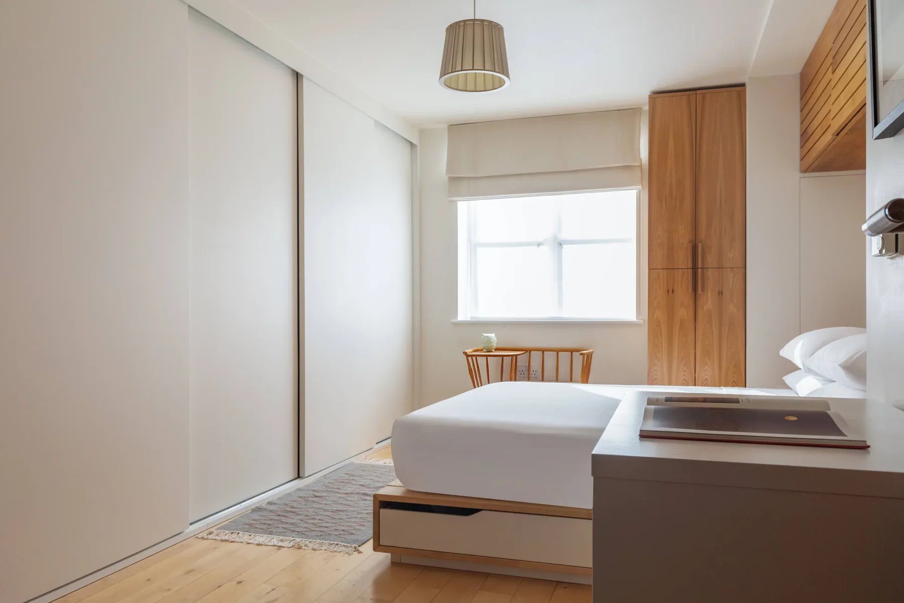 Un dormitorio luminoso con una cama, una ventana y armarios de madera.