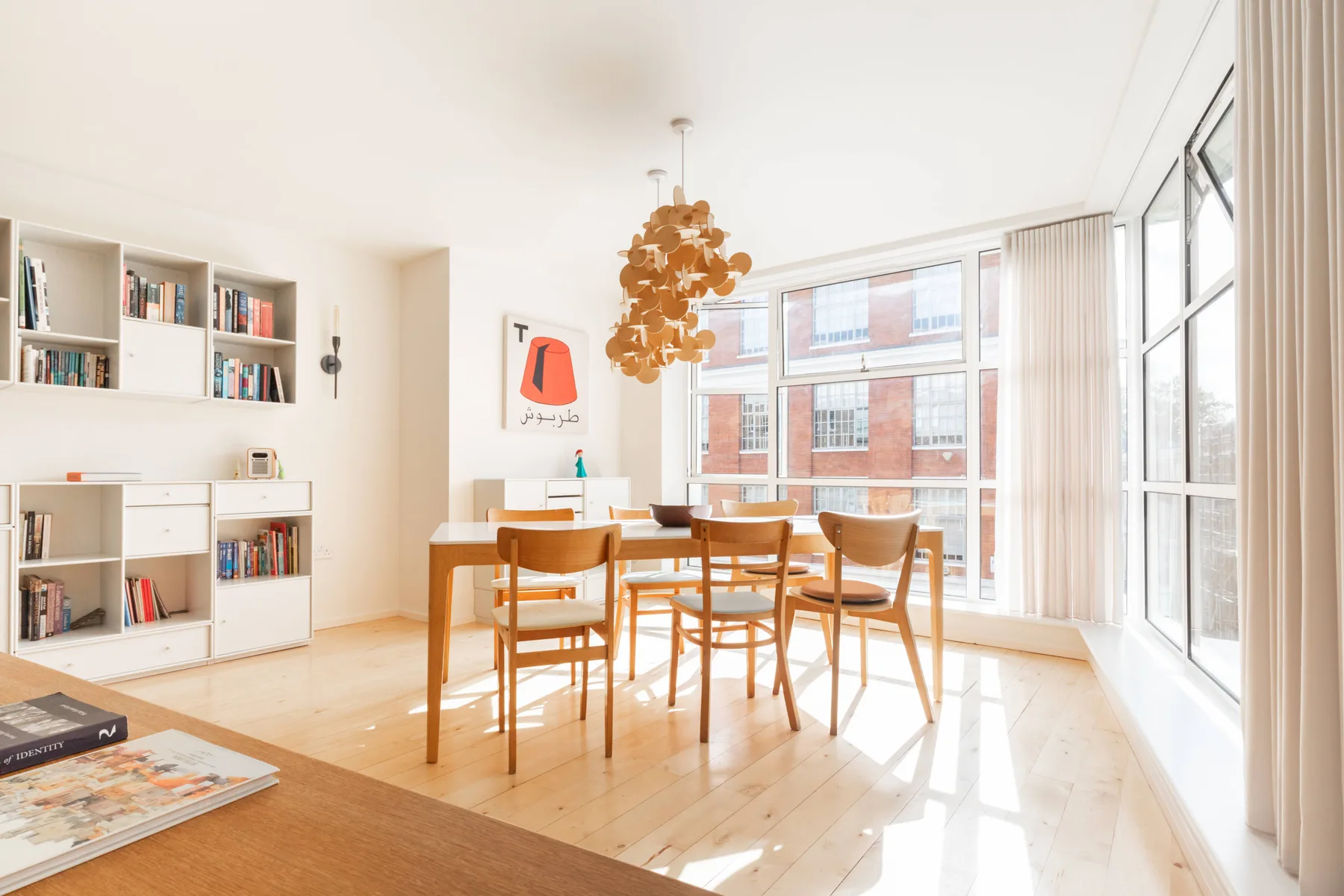 Un comedor luminoso con una mesa de madera, asientos y ventanas grandes.