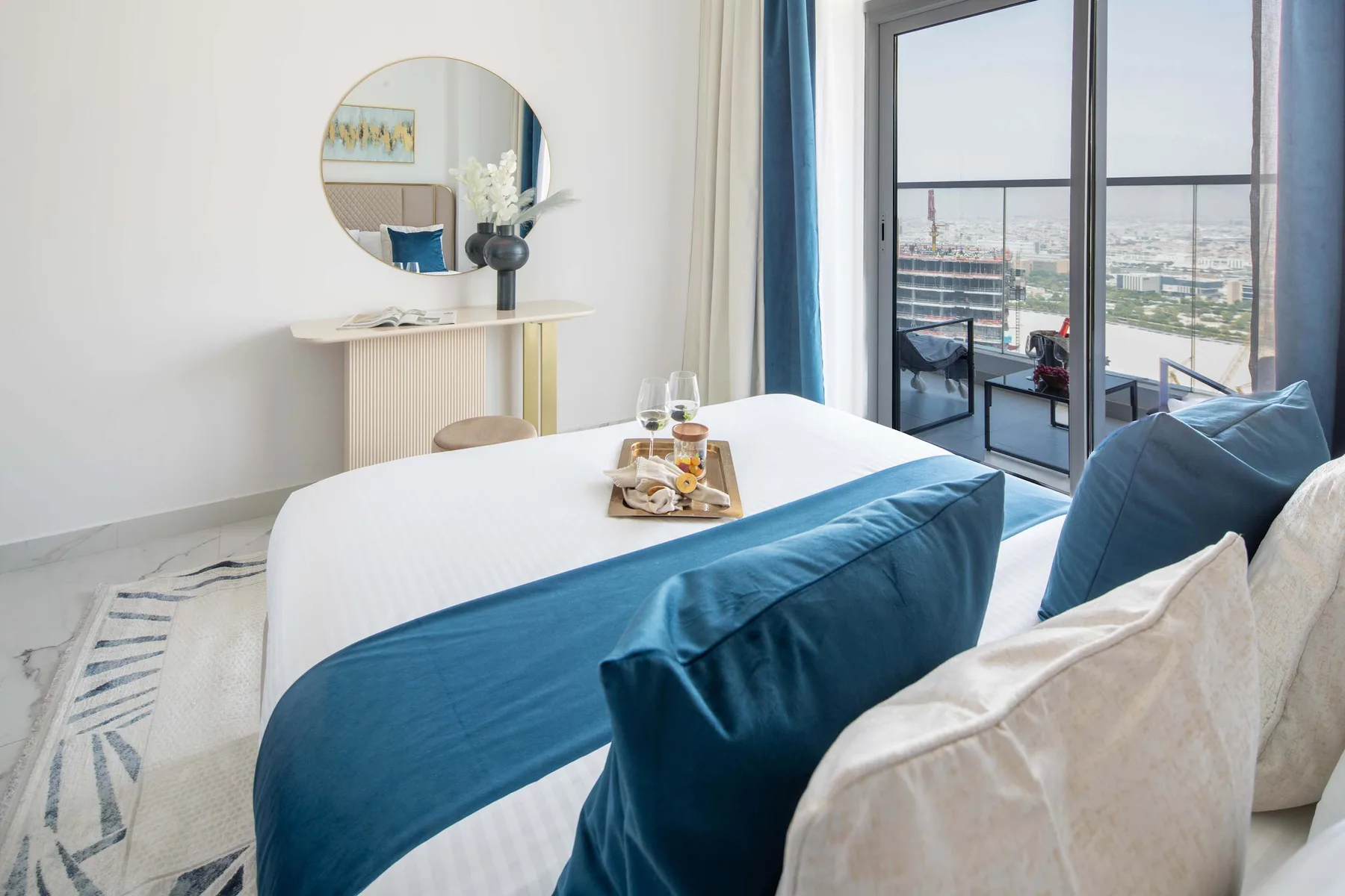 A bedroom with a neatly made bed, blue bedding, and large windows.