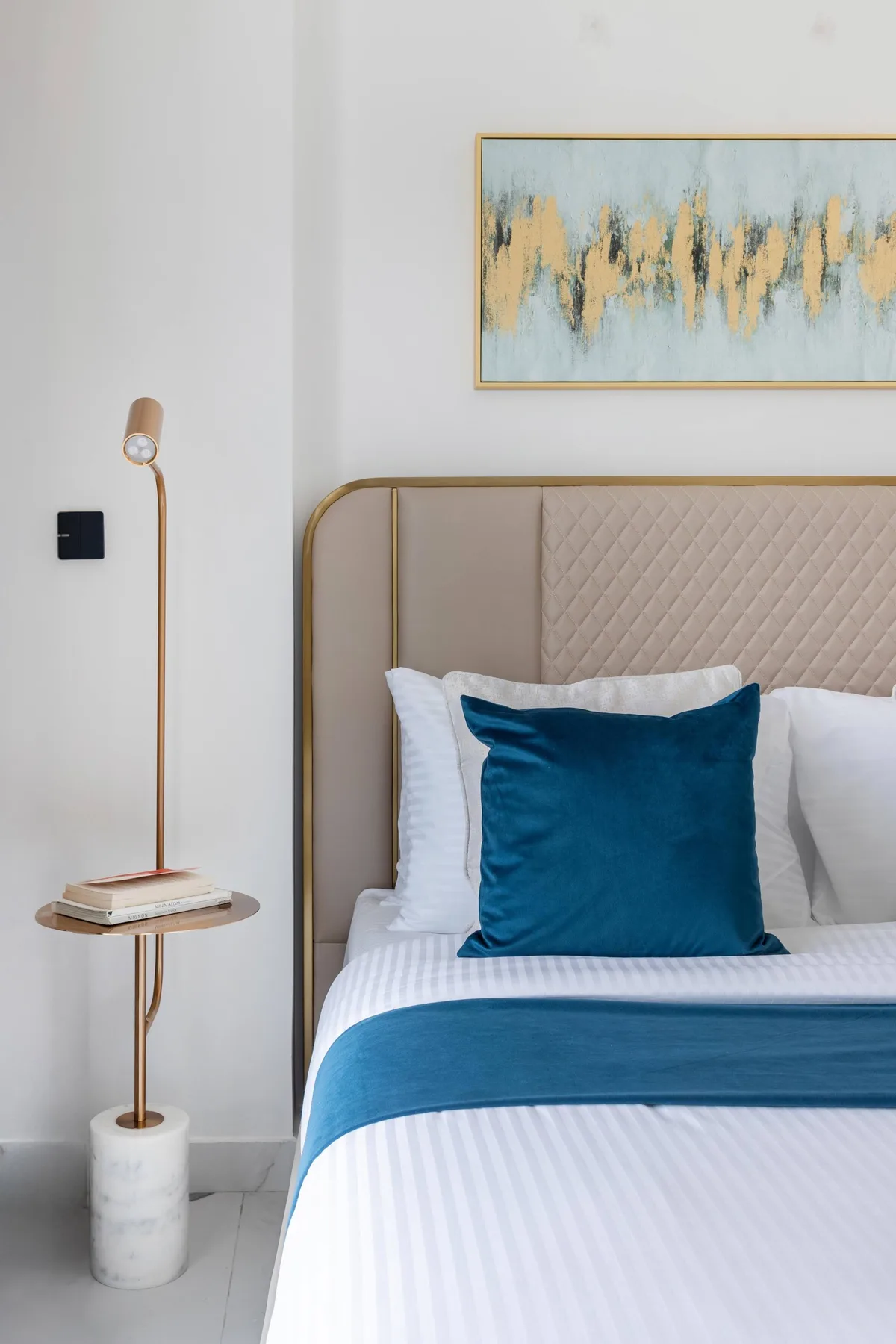 A bedroom with a neatly made bed, teal accents, and abstract wall art.