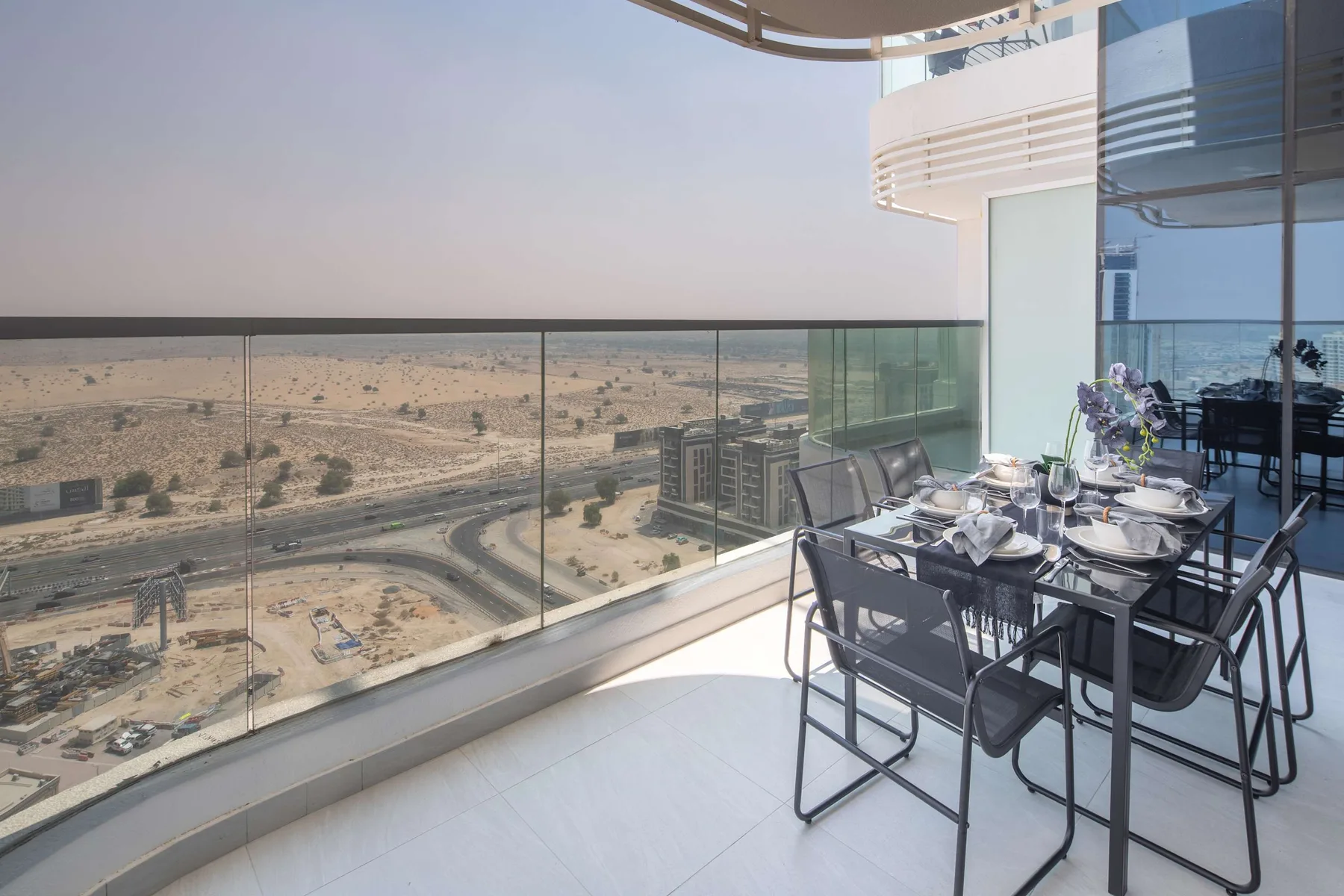 A balcony dining area with a glass railing overlooks a dry landscape.