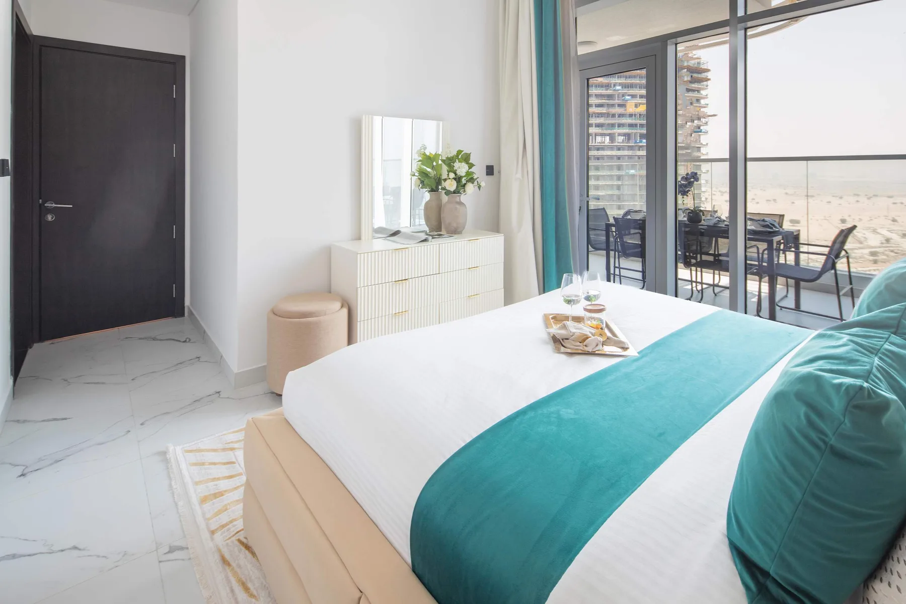 A bright bedroom with a bed, turquoise bedding, and glass doors opening onto a balcony.