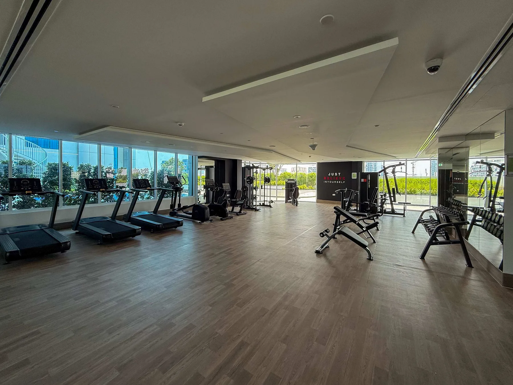 A spacious gym with treadmills and weight-training equipment beside large windows.