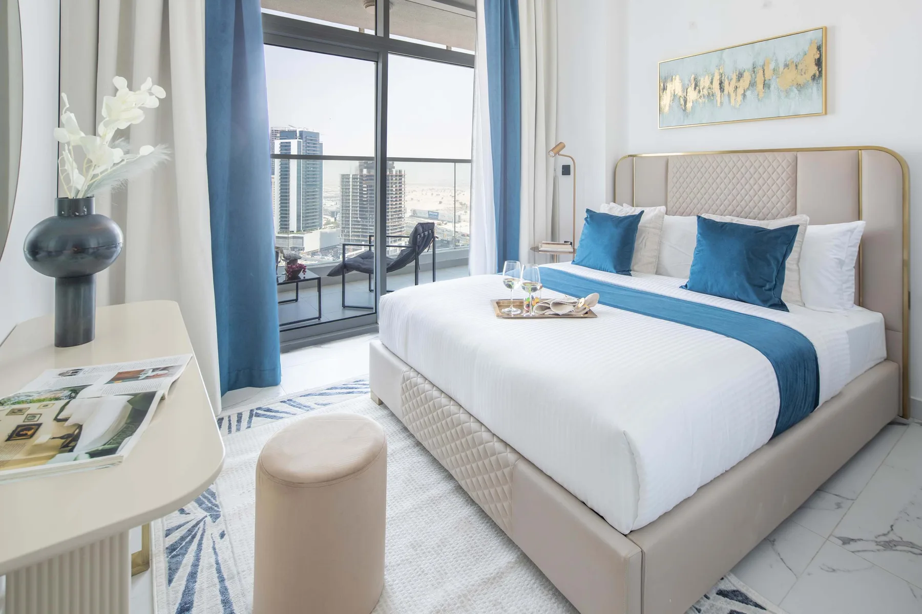 A bright bedroom with a neatly made bed and large windows overlooking the city.