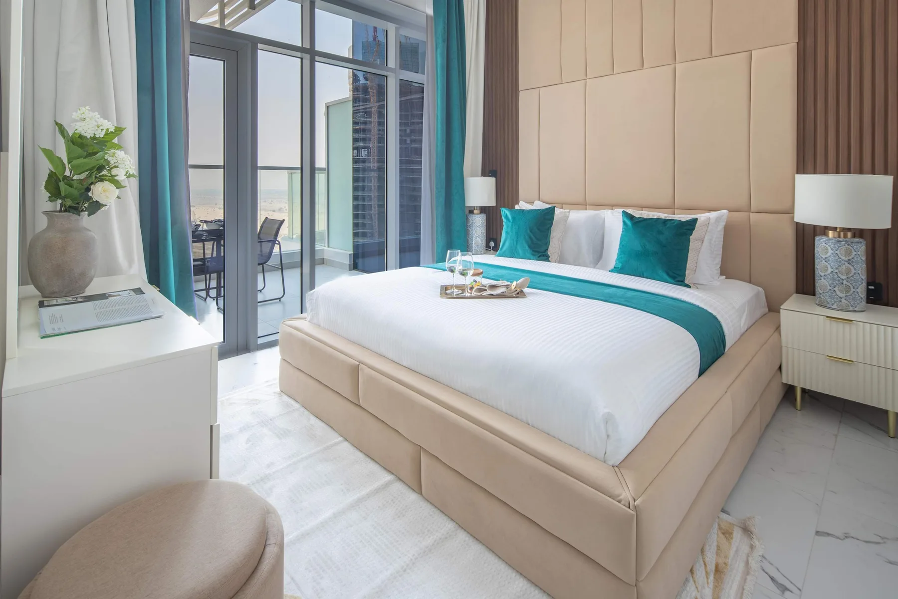 A bright bedroom with a neatly made bed and tall windows opening onto a balcony.