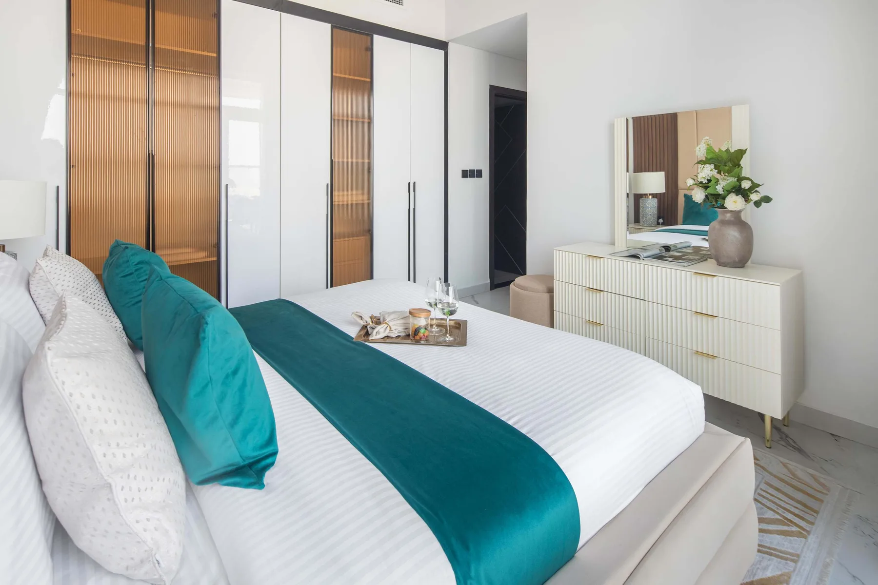 A bright bedroom with a neatly made bed and teal bedding.