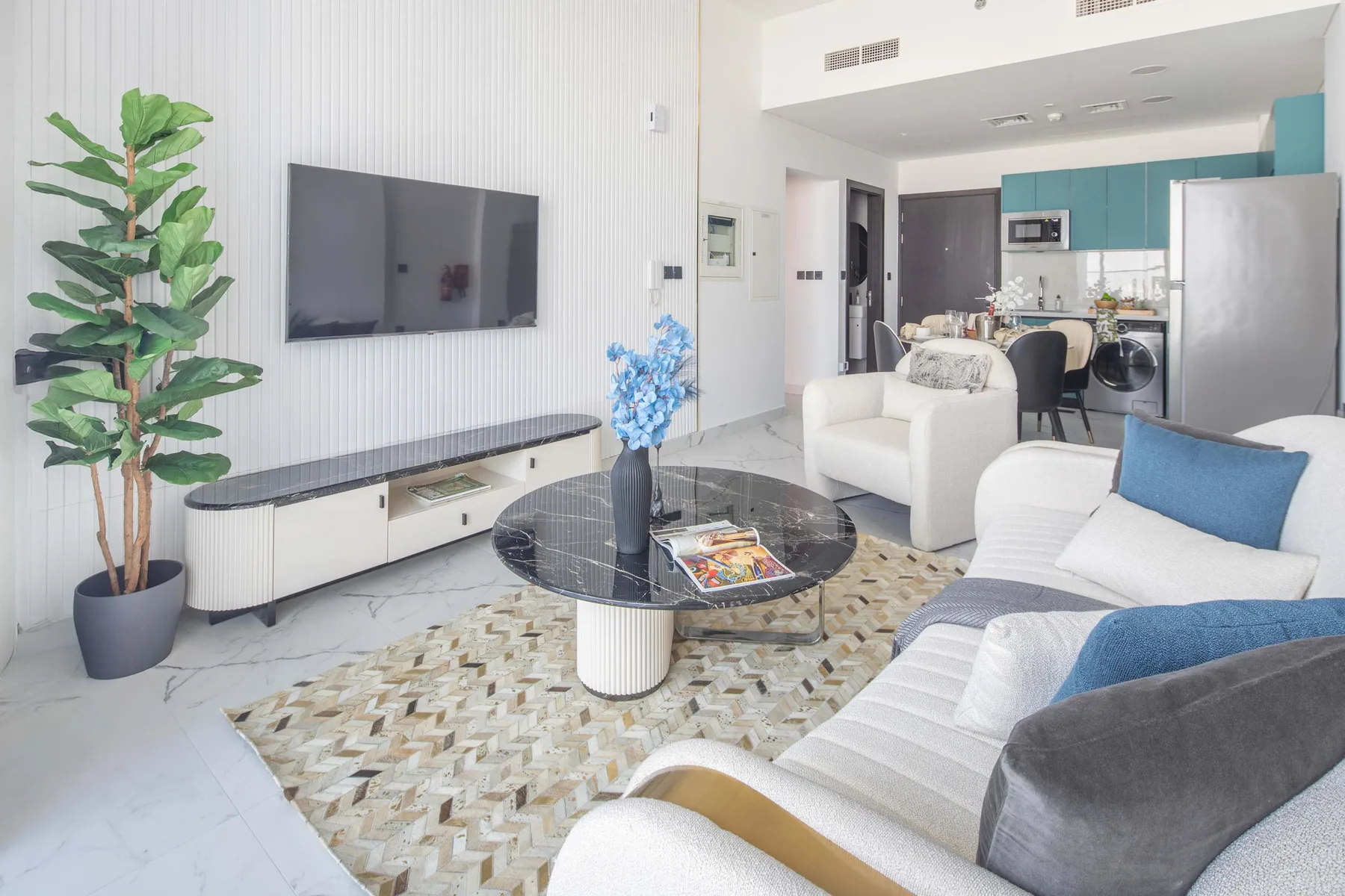 A bright living room with seating, a television, and an open kitchen.