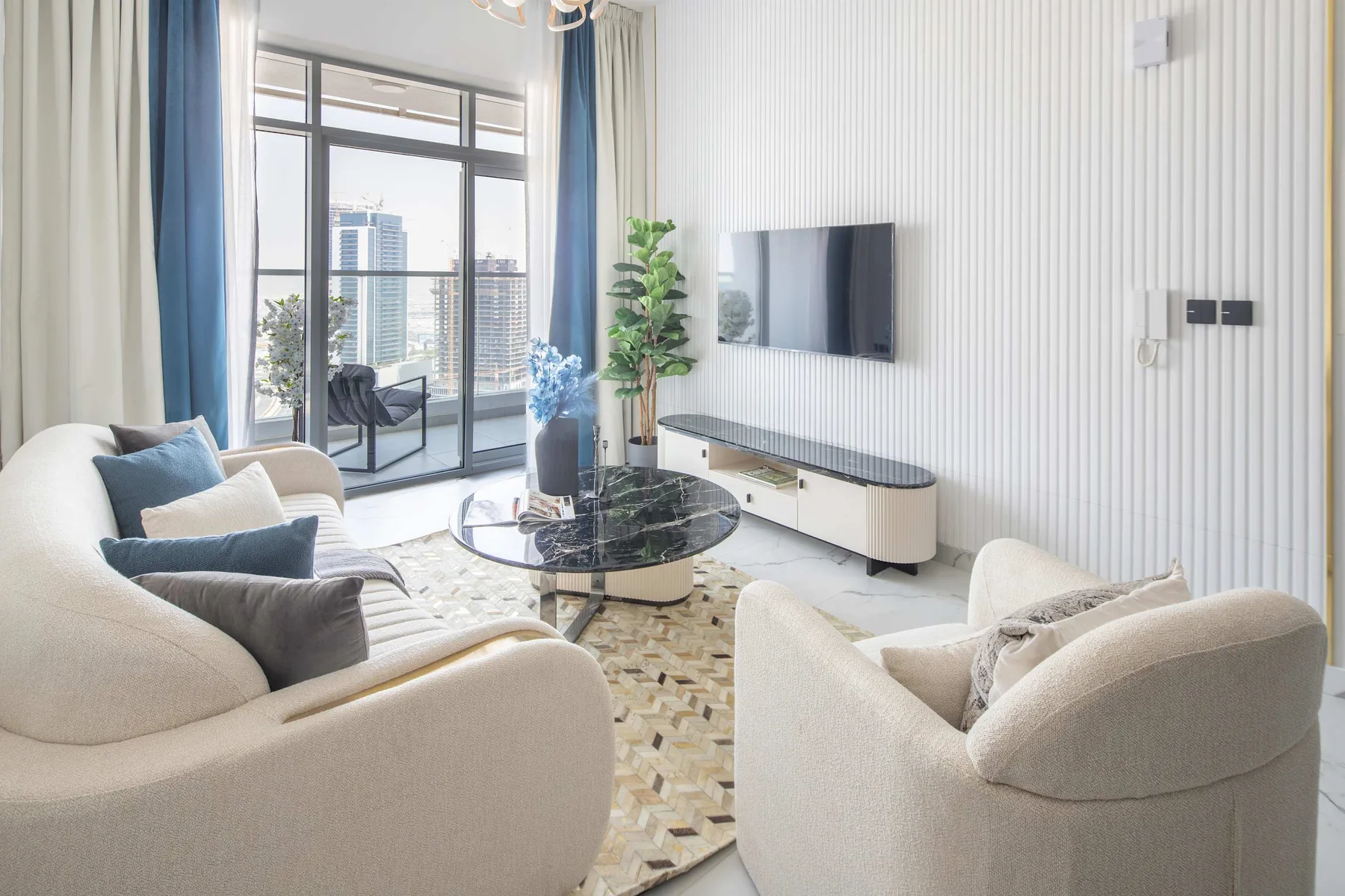 A bright living room with seating, a glass coffee table, and a wall-mounted television.