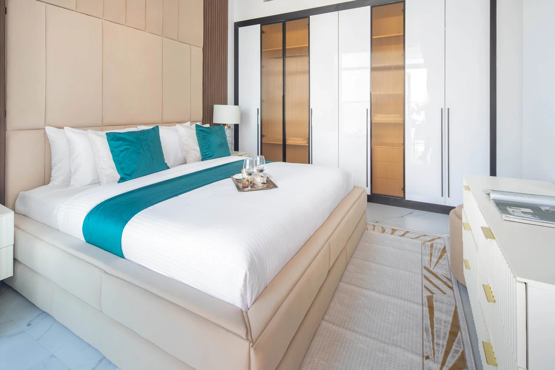 A bedroom with a neatly made bed and teal accent pillows.