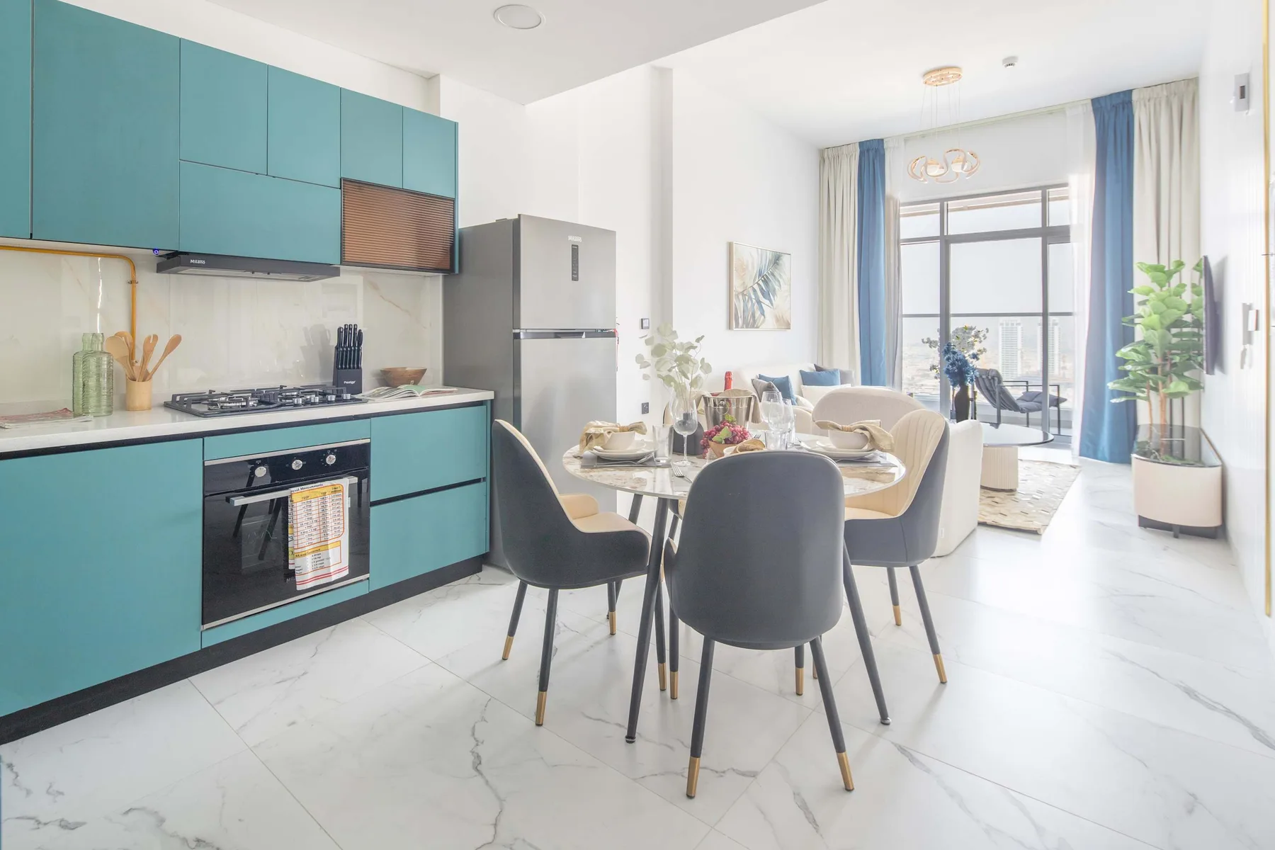 A bright open-plan kitchen and dining area with teal cabinetry and a table.