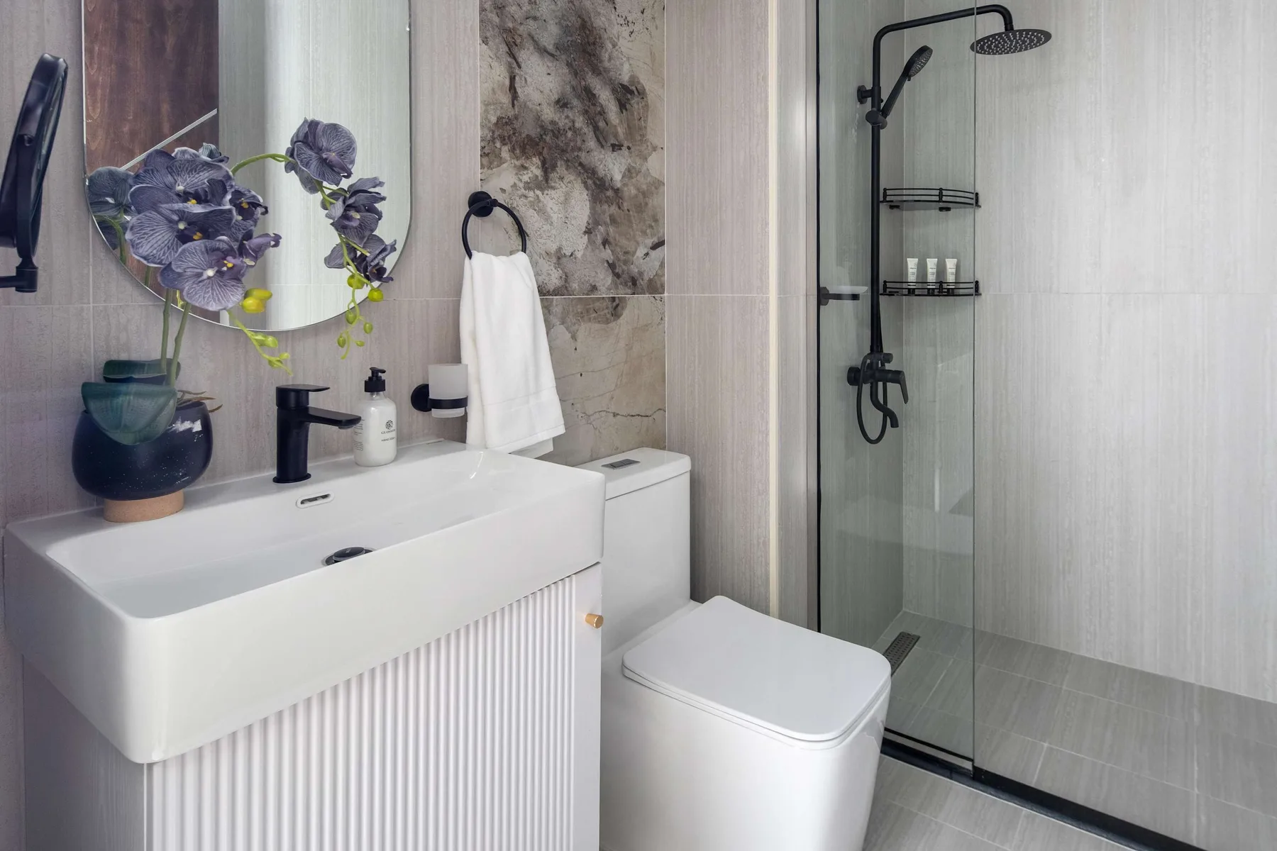 A modern bathroom with a white vanity, toilet, and glass shower.