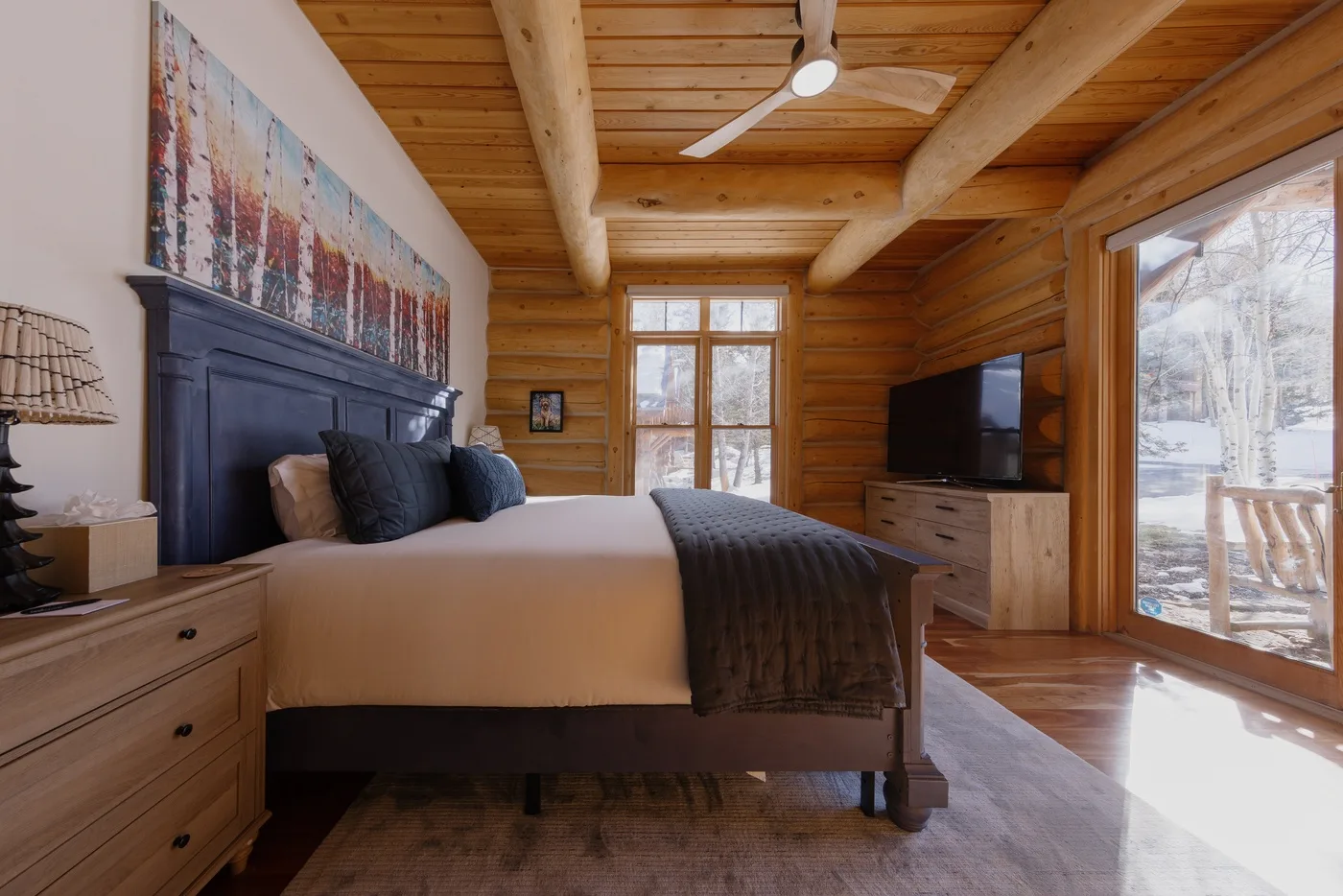 Dormitorio de cabaña de troncos con una cama, techo de madera y puertas acristaladas al exterior.