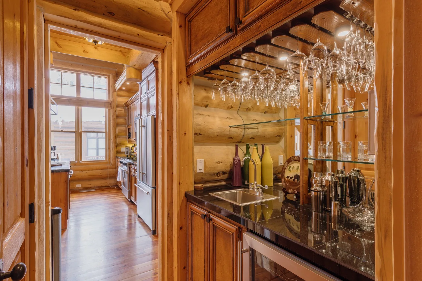 Una cocina y zona de bar revestidas de madera, con cristalería sobre la encimera.